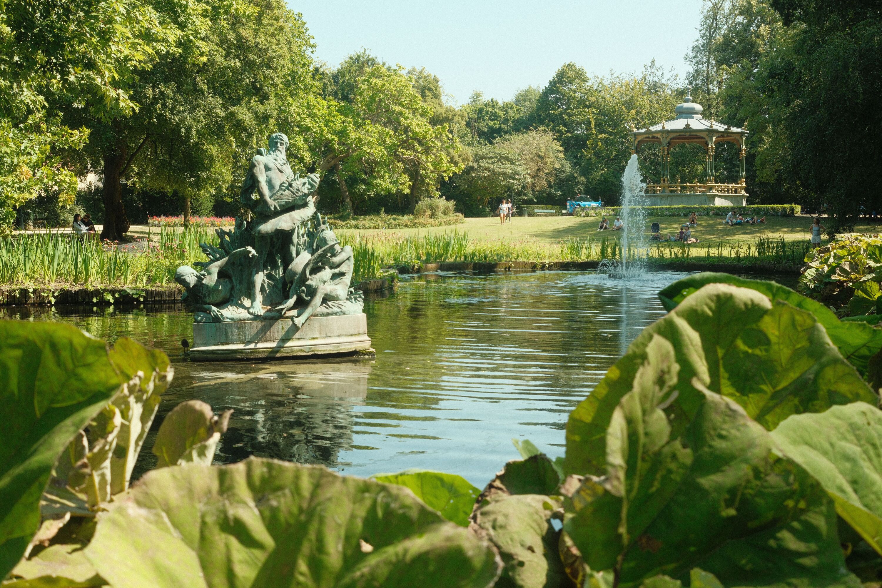 A statue in a small lake in a park during summertime.